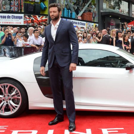 Hugh Jackman in a black suit infront of his car